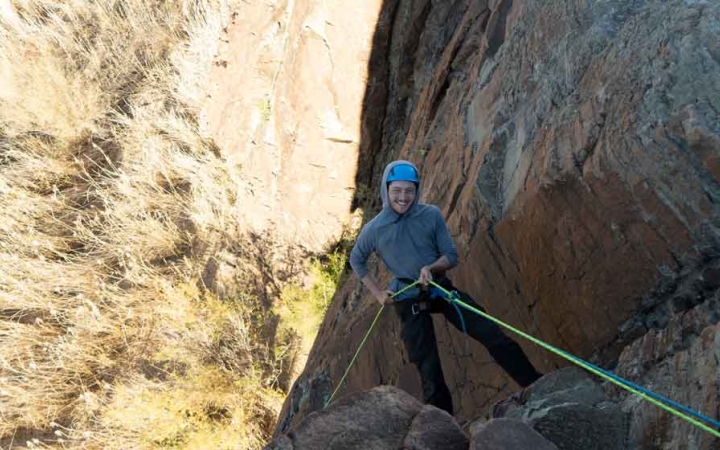 a gap year student who is rock climbing above a desert landscape looks up and smiles